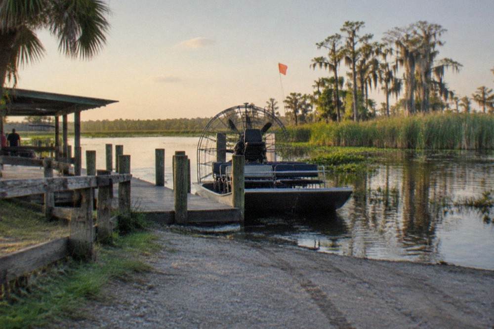 An airboat with its orange safety flag parked at a wooden dock on a Central Florida lake