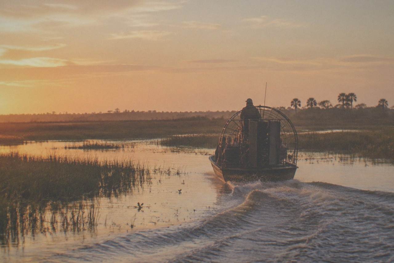 An airboat gliding across a wide open Central Florida marsh at golden hour