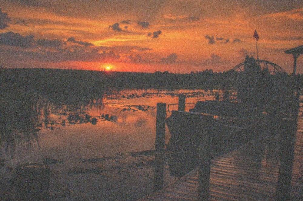a wide marsh at dusk with dark water reflecting an orange sky