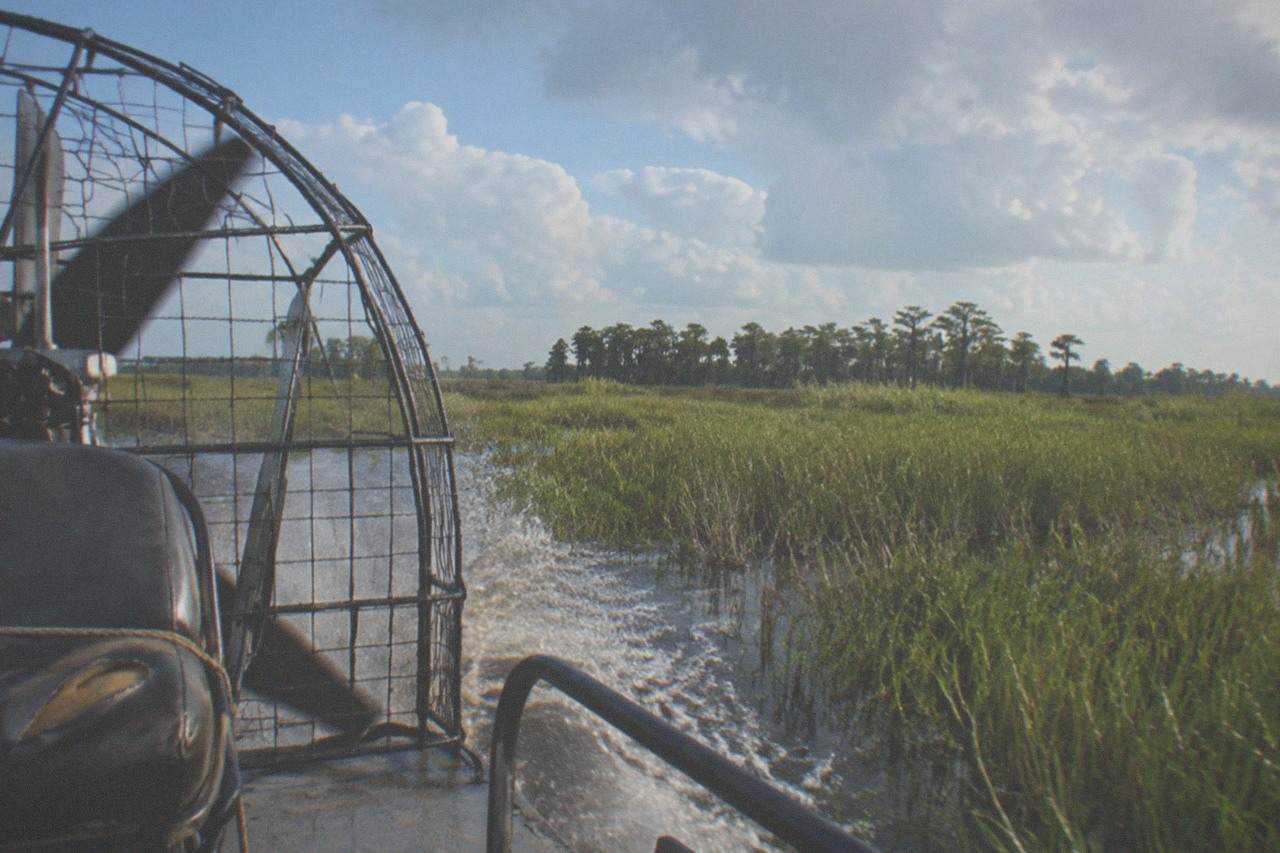 an airboat cruising across open marsh grass toward a distant treeline
