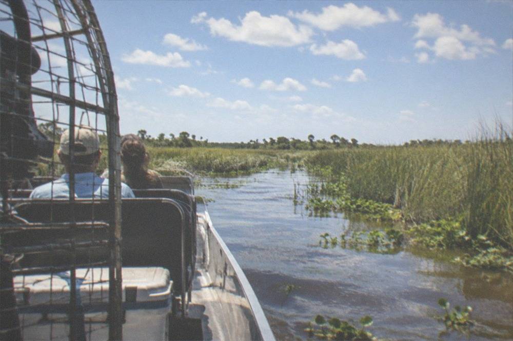 Passenger airboat cruising through open water between walls of tall marsh grass