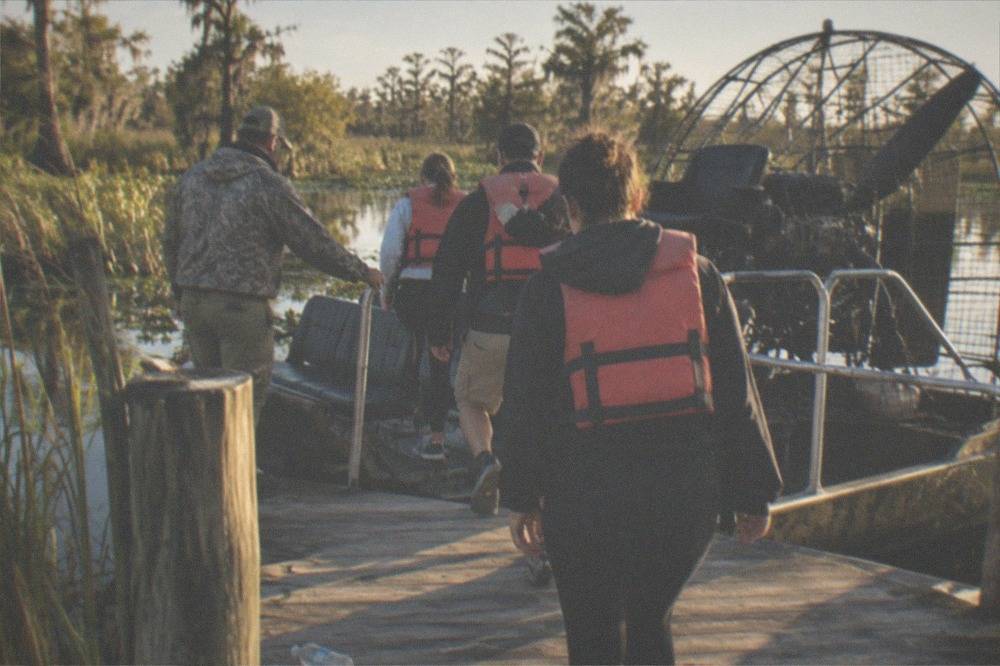 Passengers in life vests boarding an airboat at a wooden dock