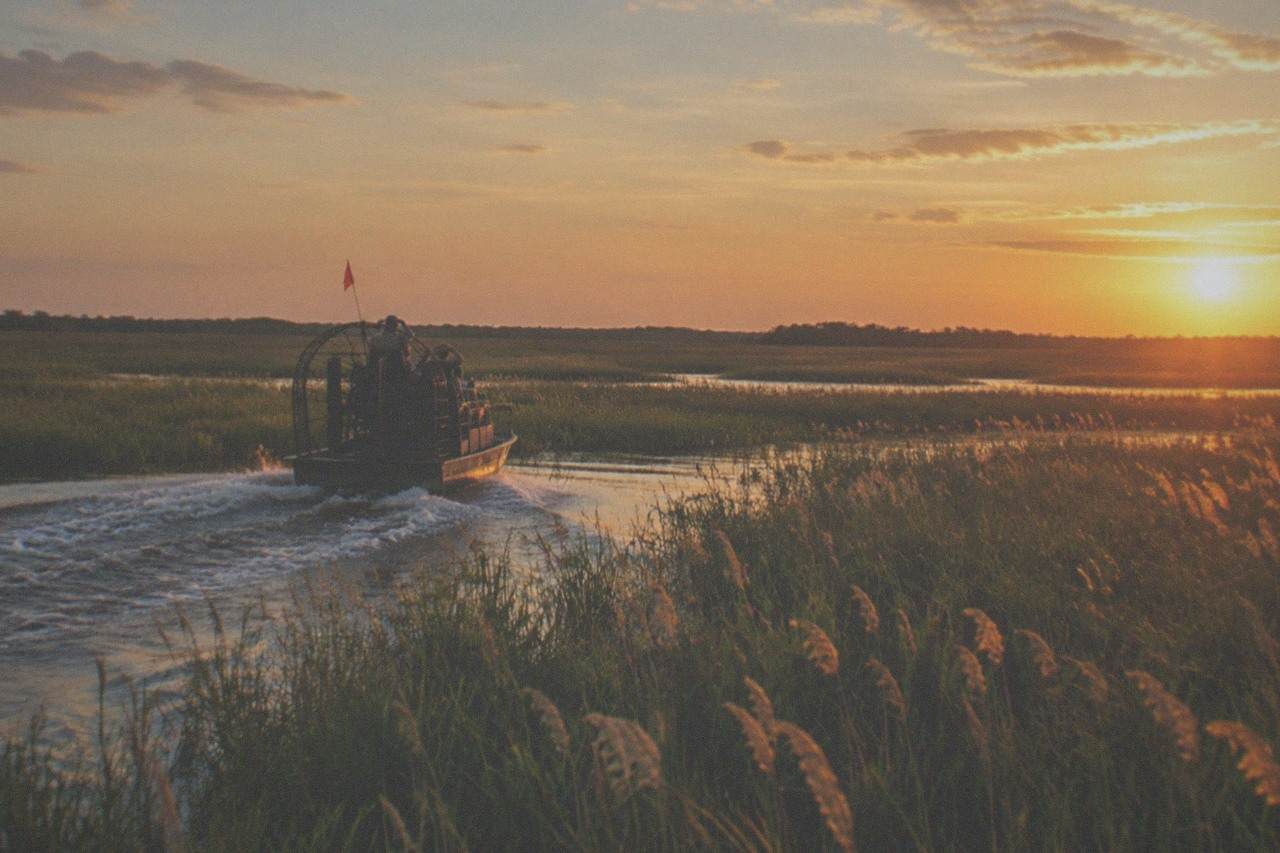 An airboat gliding across open Florida marshland at golden hour