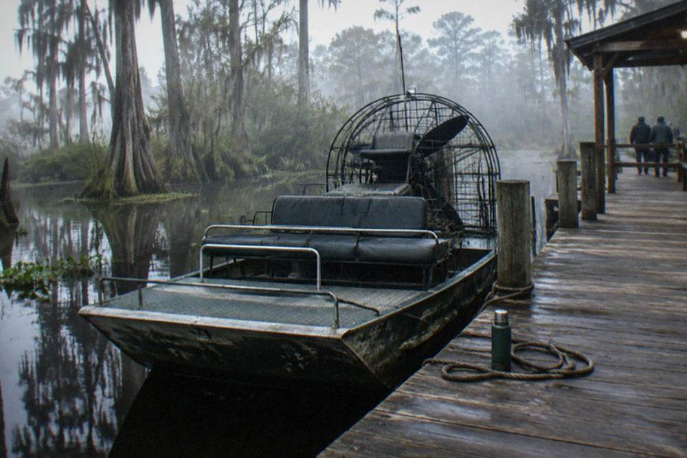 An airboat resting at a wooden dock among cypress trees and still water