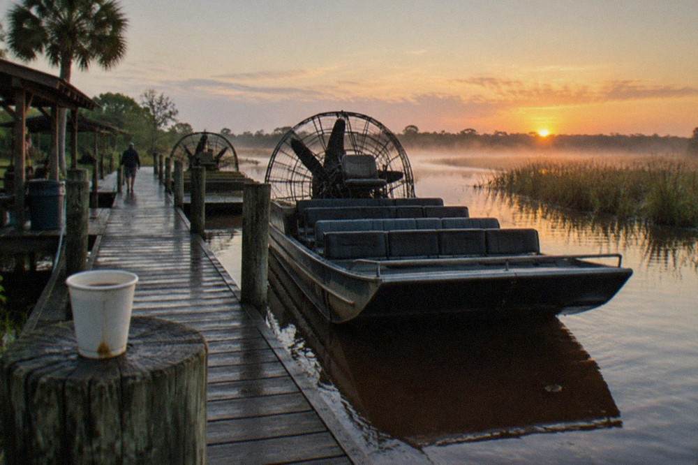 Wooden airboat dock stretching into a calm lake at sunrise with marsh grass in the background