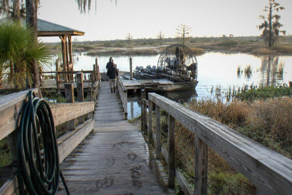 A wooden ramp leading to an airboat dock with marsh grass and low water visible