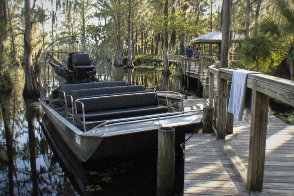 Airboat parked at a wooden dock beside a swamp boardwalk