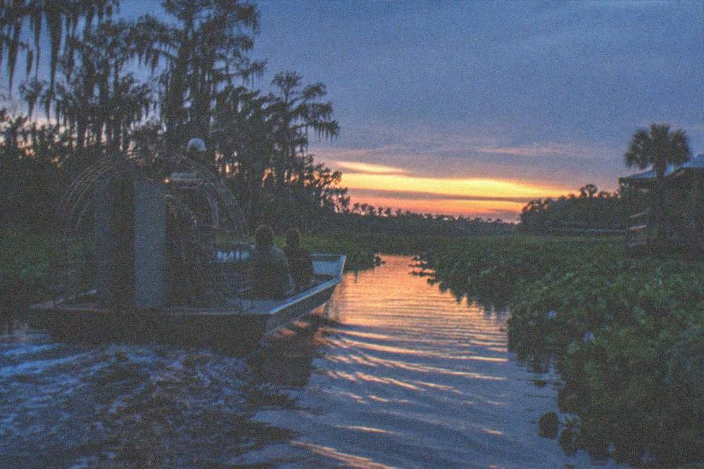 Small airboat on a narrow marsh channel at dusk