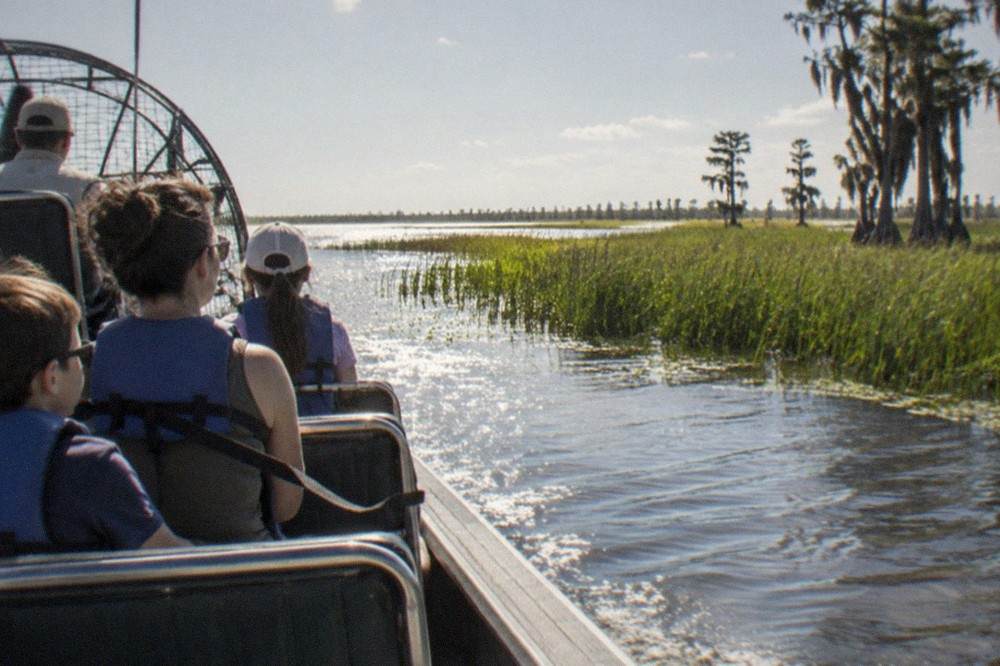 A family airboat cruising past tall marsh grass along a Kissimmee lake shoreline