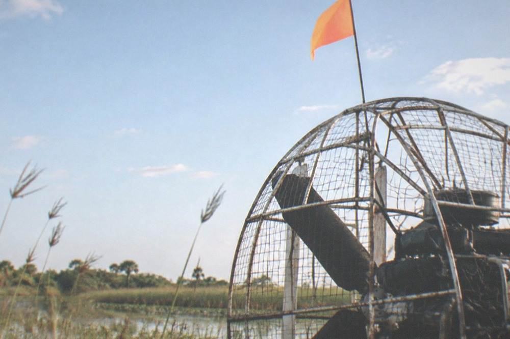 A muffled airboat engine with an orange safety flag flying from a mast above the marsh