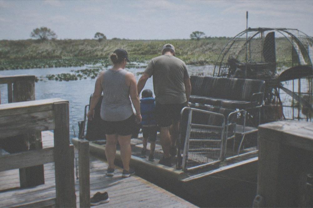 Family with a small child in a life jacket boarding an airboat at a wooden dock