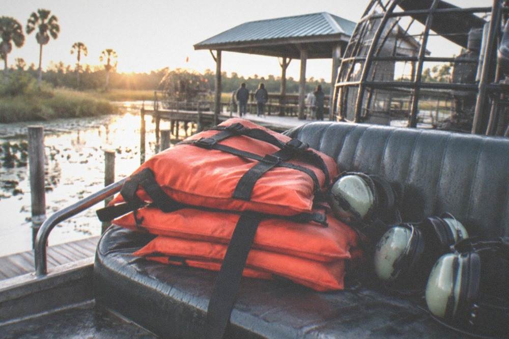 A stack of orange Coast Guard approved life vests and a set of ear protection headsets laid out on an airboat bench seat