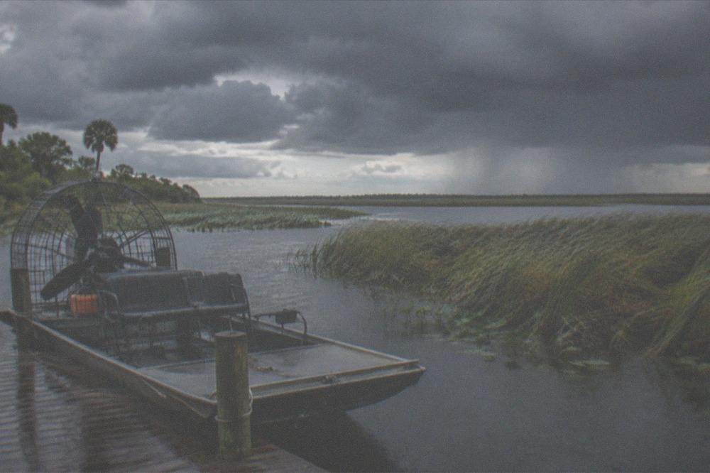 Dark storm clouds building over a Florida marsh with an airboat docked in the foreground at the edge of tall grass