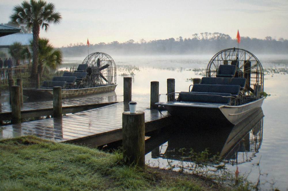 A dock with parked airboats and still water in the early morning