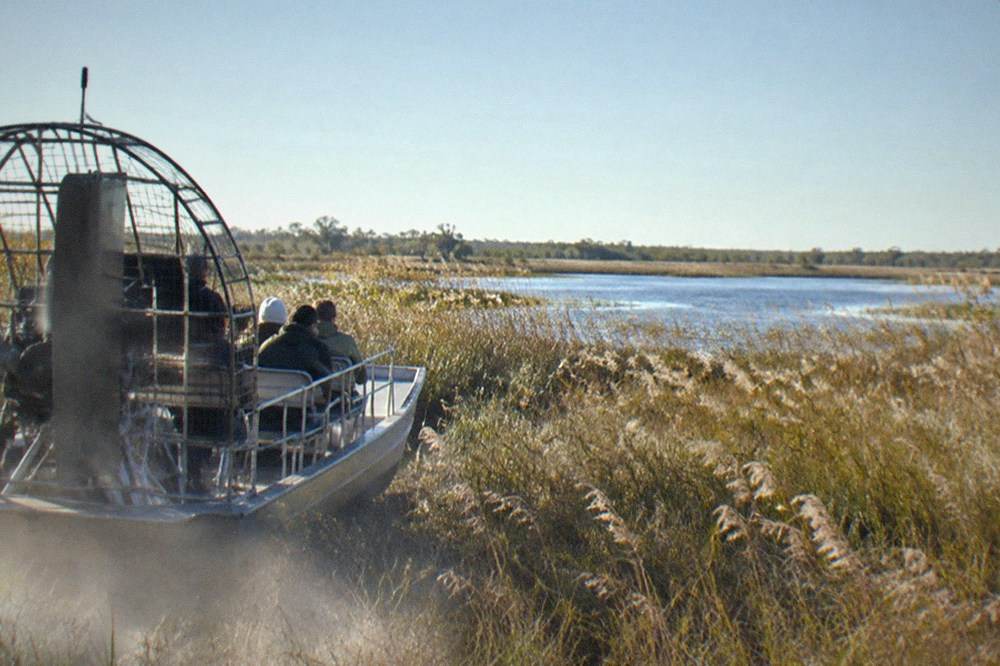 An airboat cutting through tall dry marsh grass toward open water