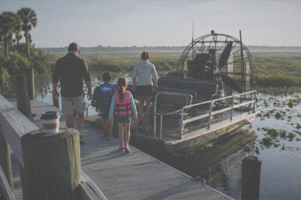A family boarding an airboat at a wooden dock in the morning