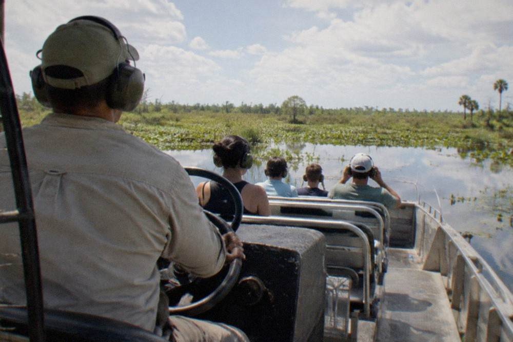 Airboat captain standing at the wheel as passengers settle into their seats
