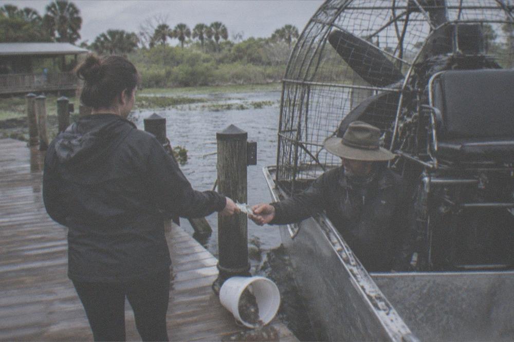 Passenger handing cash to an airboat captain beside the dock