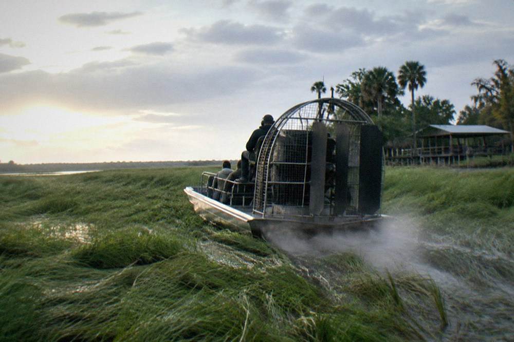 Airboat moving through open marsh grass toward a brightening sky after rain