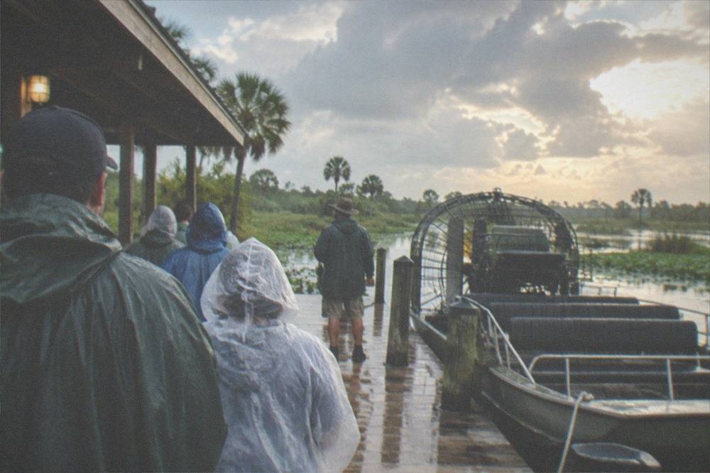 Captain and passengers in rain jackets on an airboat dock waiting under clearing skies