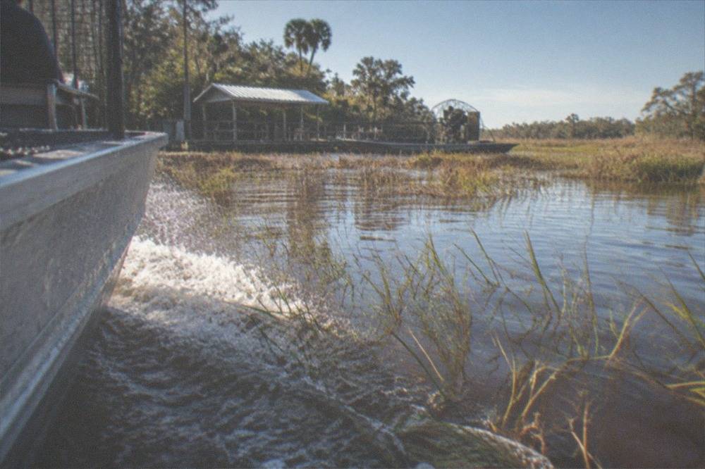 Close view of an airboat hull cutting a wake through shallow grassy water