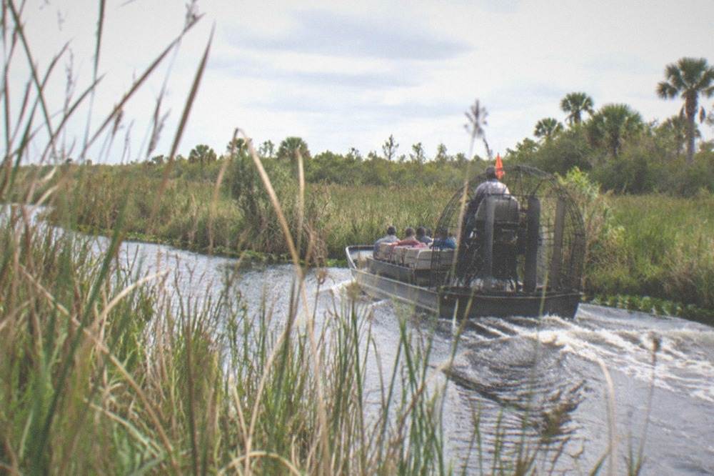 Airboat gliding through a narrow marsh channel between tall reeds
