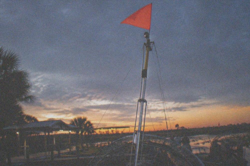 an airboat mast flying an orange safety flag against a darkening sky over water