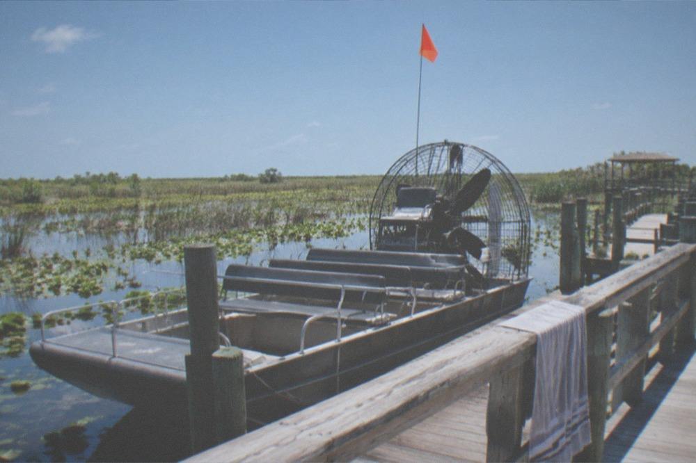An airboat parked at a wooden dock with orange safety flag raised on its mast