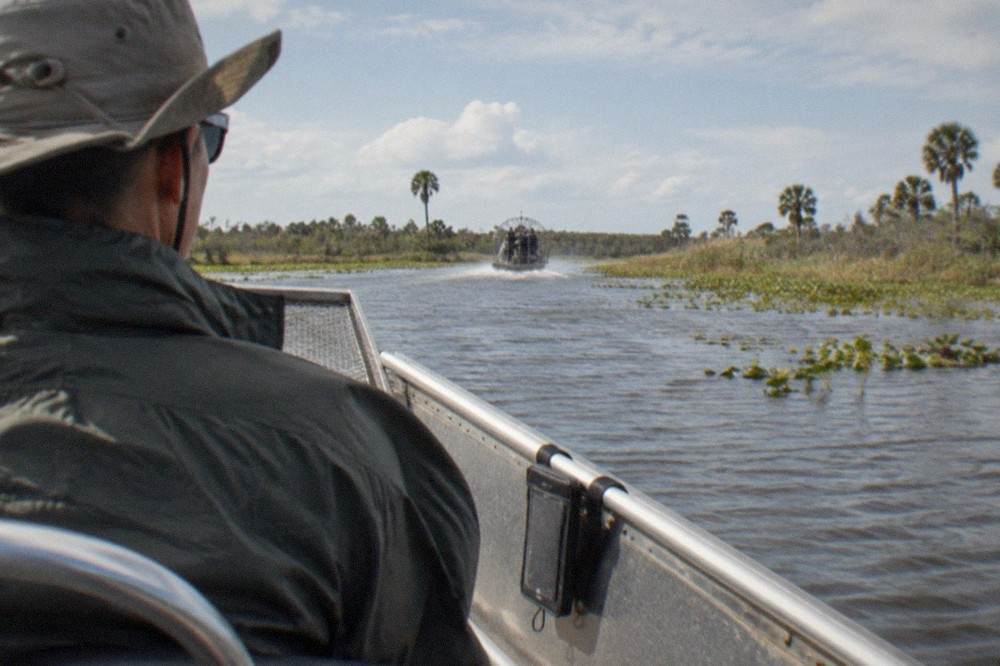 Airboat passenger wearing a strapped hat and sunglasses on an open marsh ride