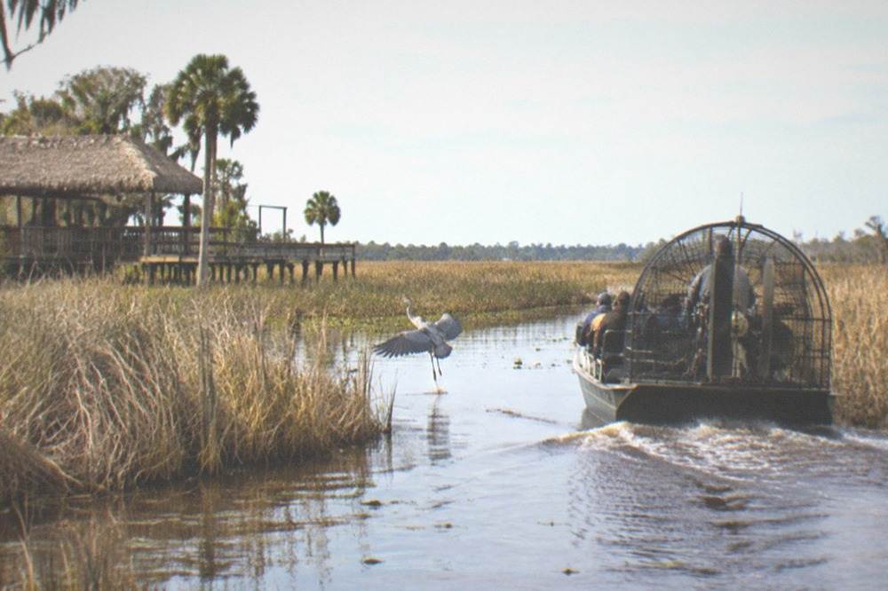 Airboat moving through narrow marsh channel with tall dry grasses under a wide winter sky