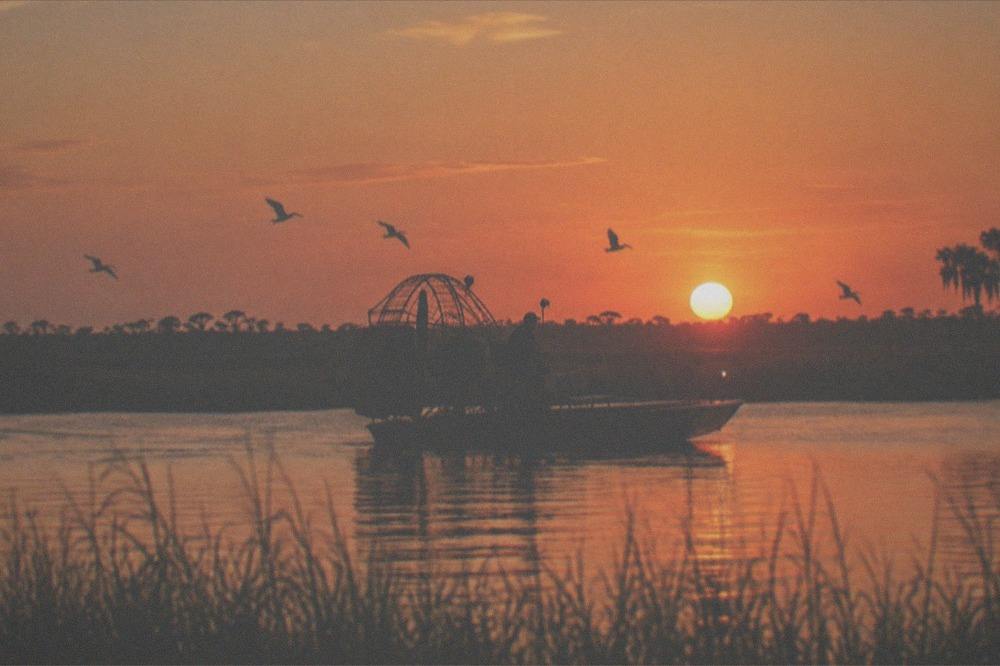 Airboat on open water at sunset with warm orange sky and silhouetted marsh grass